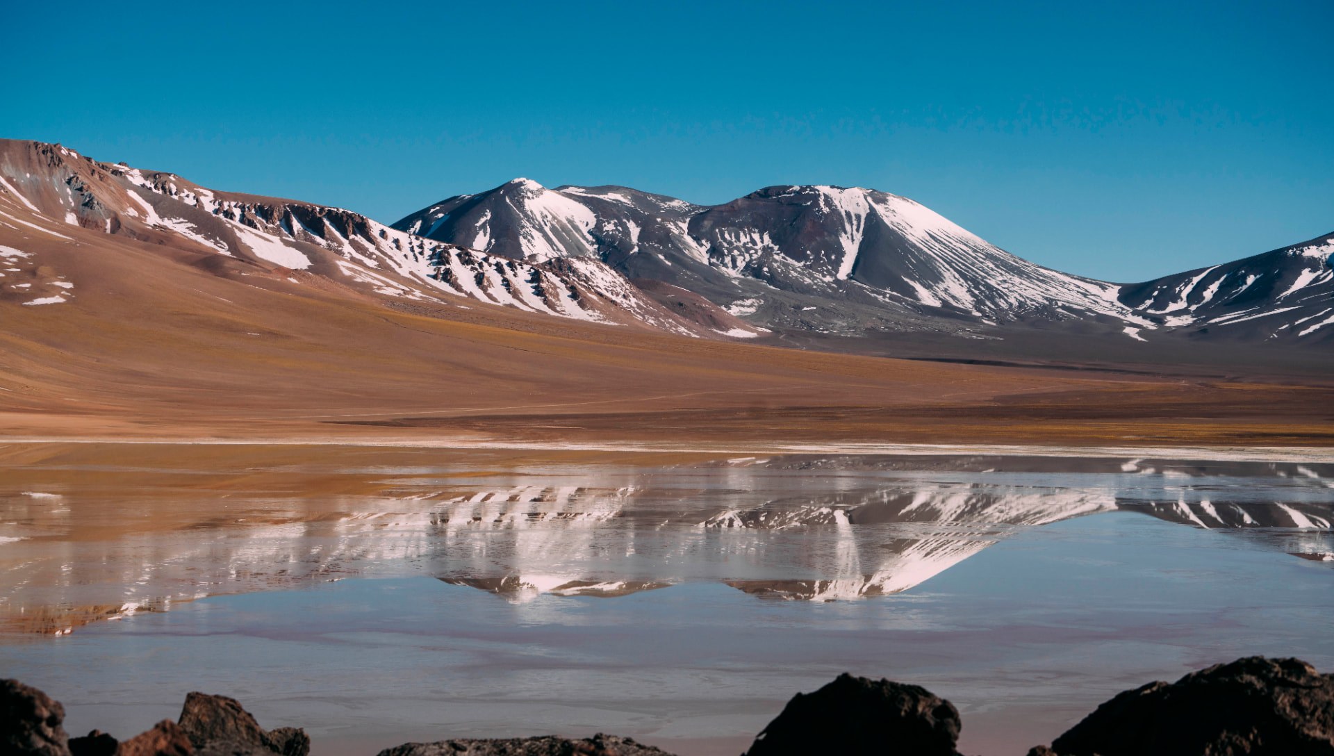 Lagoa altiplânica refletindo montanhas nevadas do Atacama