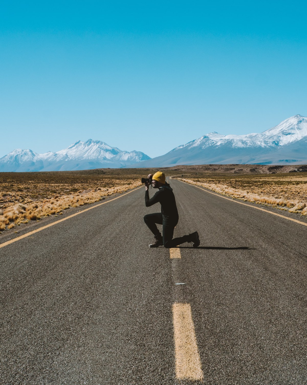 Fotógrafo ajoelhado no meio de uma estrada do altiplano fotografando os vulcões