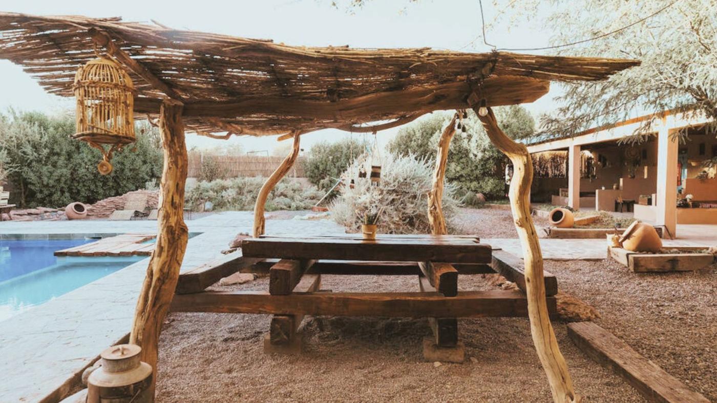Mesa de madeira sob pergolado de totora ao lado da piscina