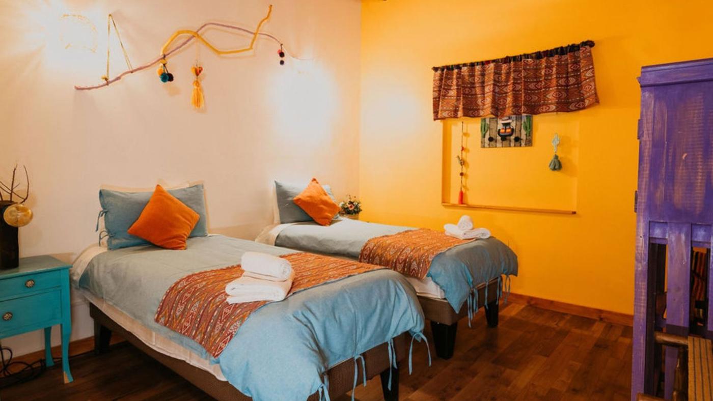 Quarto duplo com paredes amarelas e têxteis andinos