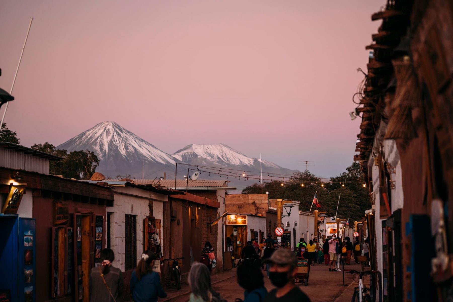 Rua de San Pedro de Atacama ao entardecer com vulcões nevados ao fundo